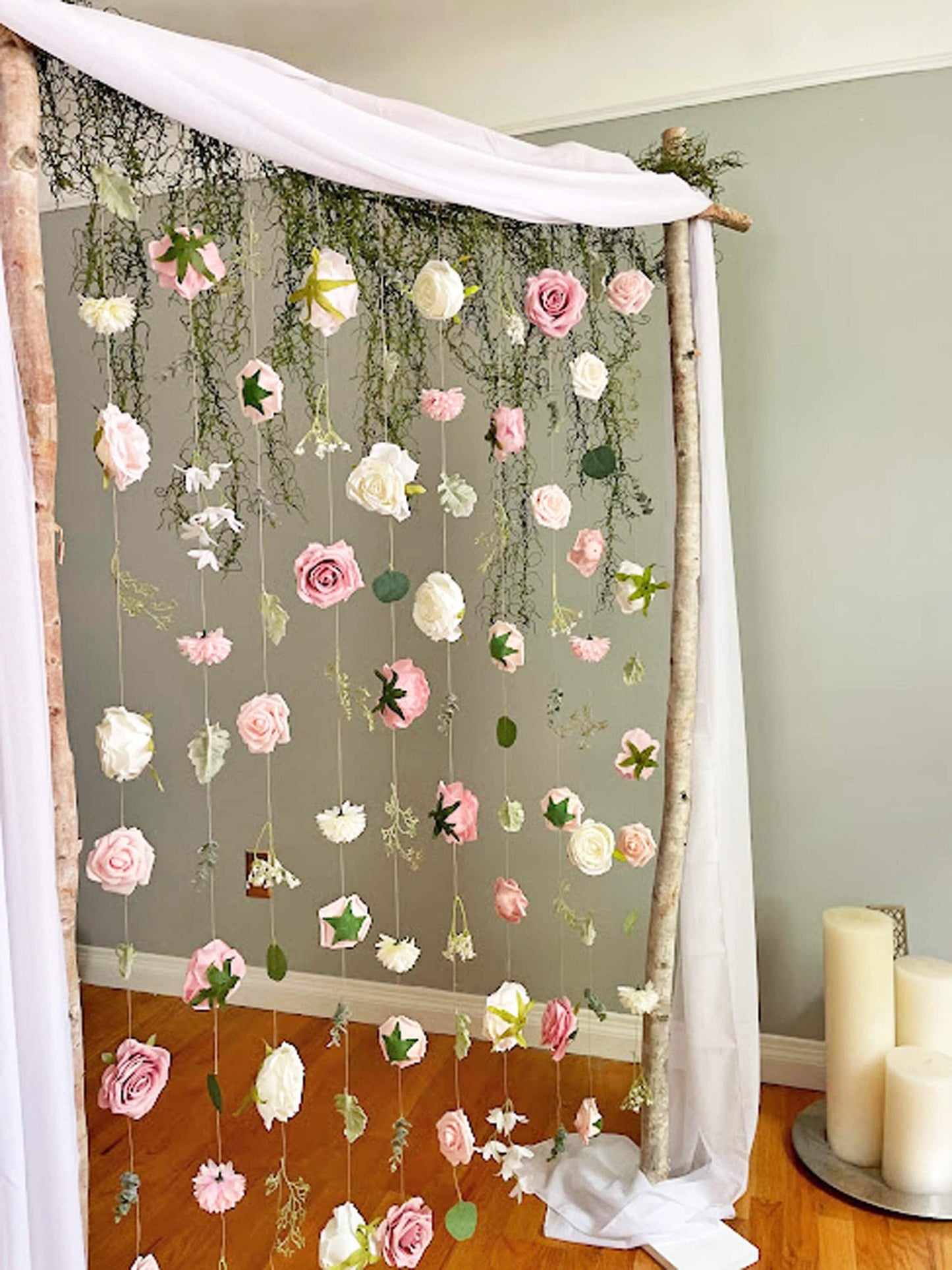 Floral string curtain hanging from a birch wedding arch with candles and greenery in a studio setting.