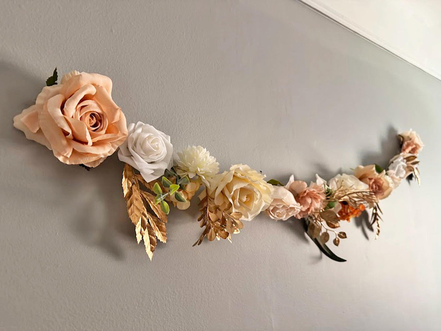 Nude, gold and ivory flower garland hanging on gray wall
