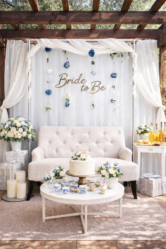 Decorated outdoor setting with floating blue flowers, 'Bride to Be' sign, white sofa, and floral arrangements.