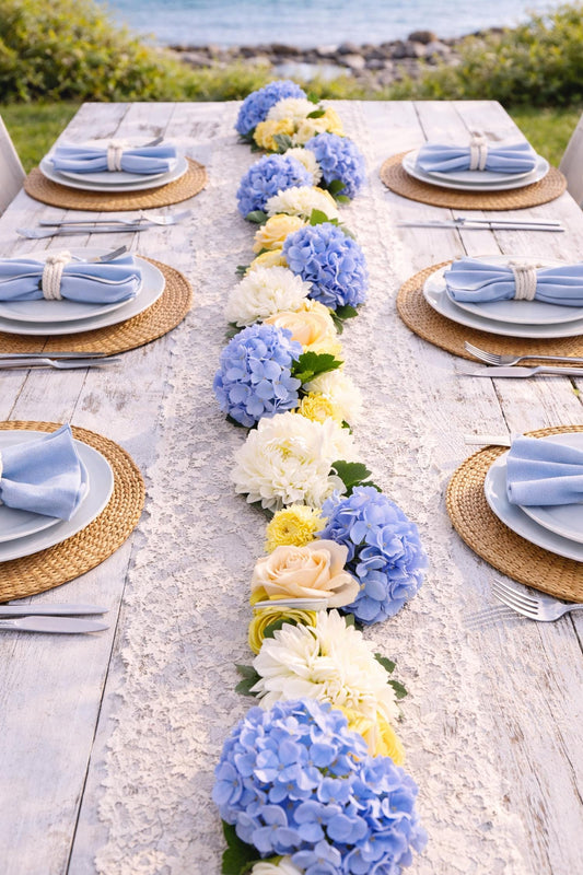 Outdoor table setting with a floral runner and blue, yellow, and white flowers.