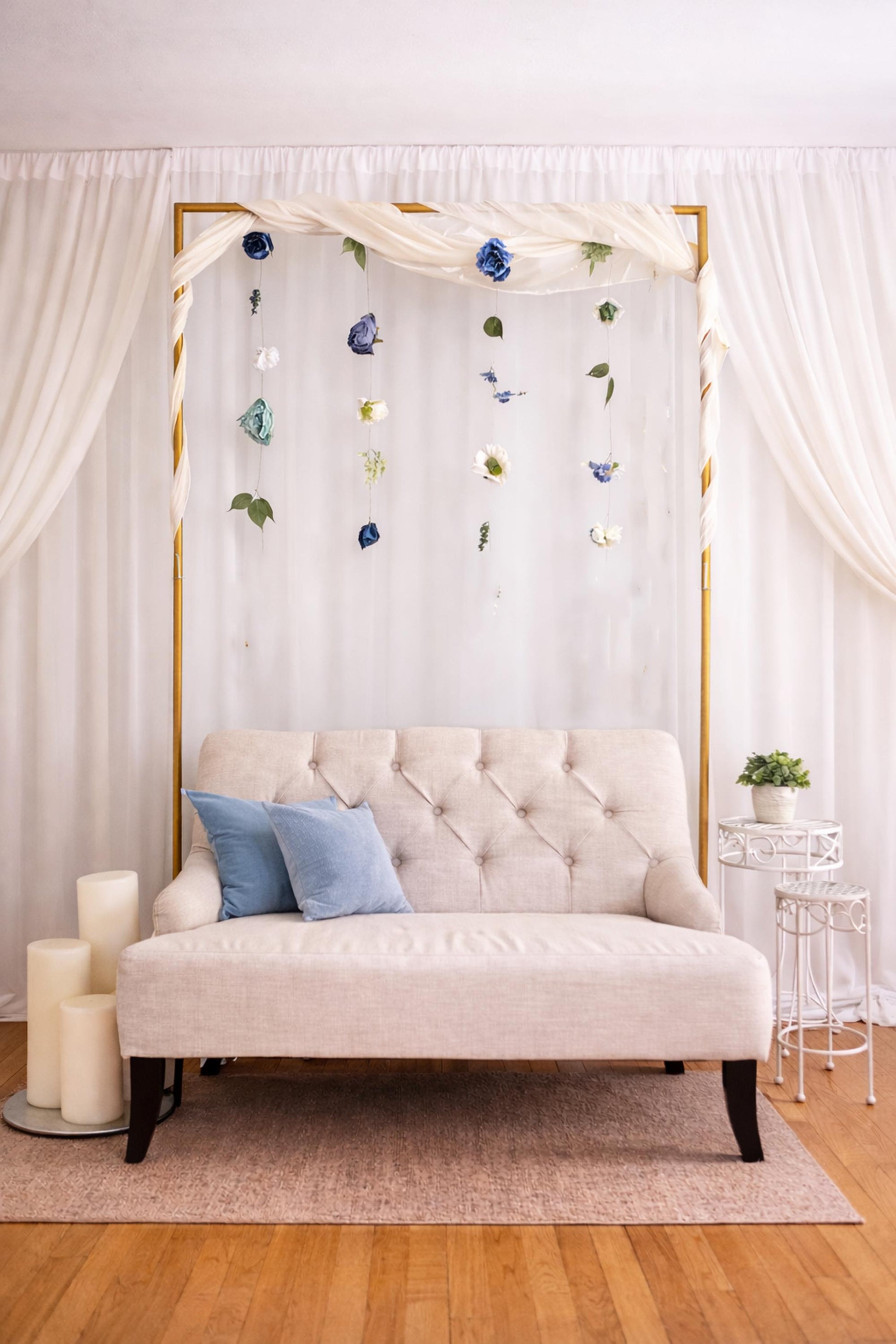 Decorative setup with a beige sofa, blue pillows, and floral arch in a room.