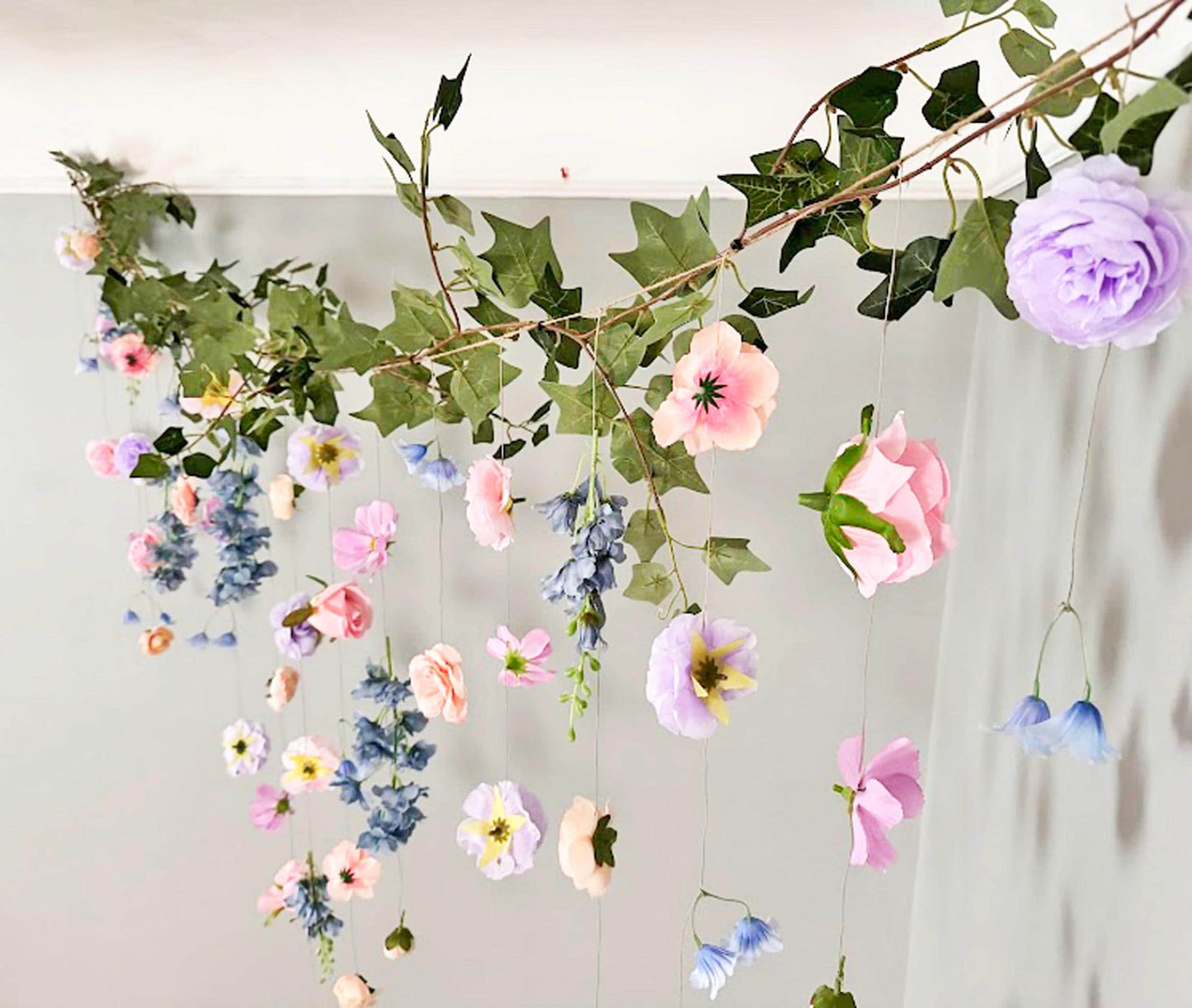 Decorative floral garland with purple, pink, peach and dusty blue flowers and green leaves on a white background.