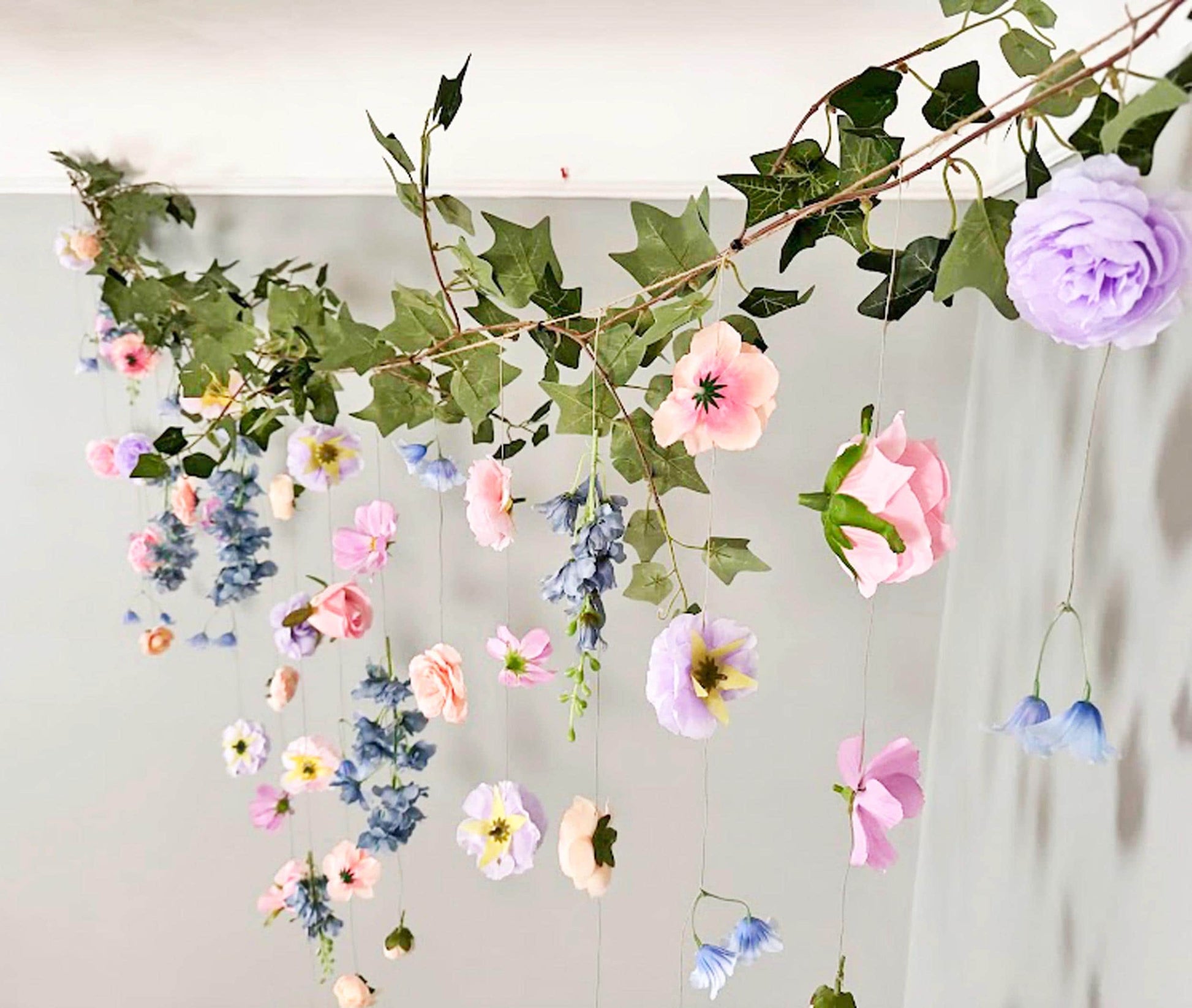 Decorative floral garland with purple, pink, peach and dusty blue flowers and green leaves on a white background.